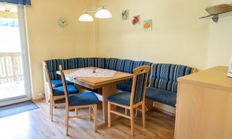 An inviting dining area with a round table and a cozy corner bench. The walls are painted in soft shades of yellow and decorated with colorful pictures.