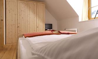 A cozy bedroom with a large bed and a wooden wardrobe. The room has a window with plenty of daylight.