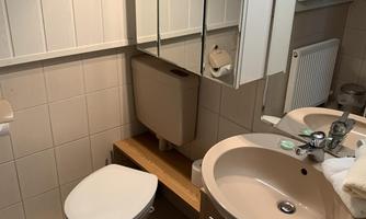 A modern bathroom with bright tiles and a sink. It features a mirror, a toilet, and a wooden cabinet.