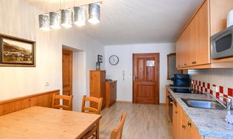 A modern kitchen with wooden cabinets and a dining table. The walls are light and the lighting creates a friendly atmosphere.