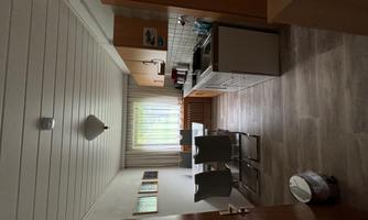 A modern kitchen with wooden cabinets and a dining table for four people. The window lets in plenty of natural light and the floor is covered with bright tiles.