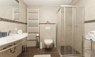 A modern bathroom with a shower, sink, and toilet. The walls are in neutral tones and there are towels as well as a radiator.