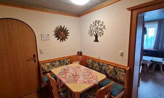 A cozy dining area with a round table and chairs. Decorative elements hang on the wall, and a table with a floral tablecloth invites you to dine.
