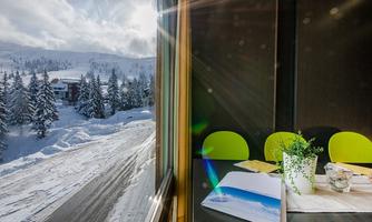 A cozy interior with a table and chairs in light green. Outside, you can see snow-covered trees and a winter landscape under a cloudy sky.