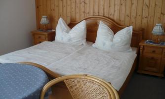 A cozy bedroom with a double bed and two large pillows. Next to the bed is a small table and a lamp.
