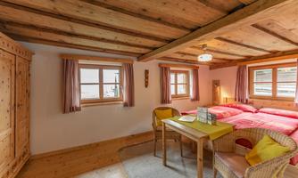 A cozy bedroom with wooden ceilings and two beds. The room has large windows and a table with chairs.