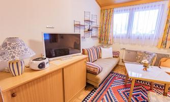 A cozy living room with a TV, a couch, and a coffee table. Colorful curtains and a carpet give the room an inviting atmosphere.