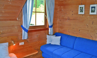 A cozy room with paneled wooden walls. A blue sofa and a window with checkered curtains create an inviting atmosphere.