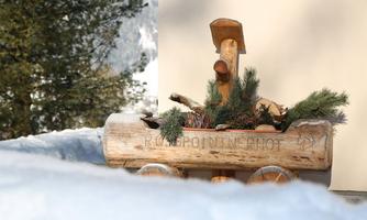 A rustic wooden sculpture adorned with green plants. In the background, snow-covered areas and trees are visible.