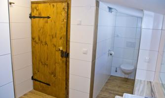 A bathroom with a wooden protective door and modern white walls. The floor is made of wood, and there is a toilet as well as a sink.