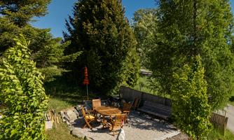A cozy outdoor area with a round table and chairs on a paved space. Surrounded by trees and green grass.