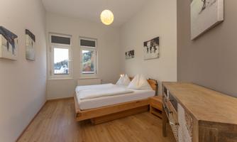 A cozy bedroom with a large bed and wooden floor. The walls are painted light and decorated with pictures.