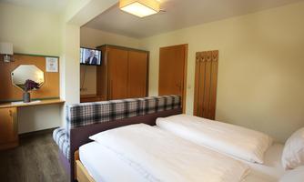 A simple and modern room with two single beds. The room is well-lit and includes a television as well as a desk.