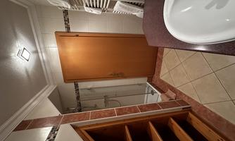 A modern bathroom with a shower, a sink, and a wooden shelf. The walls are tiled and there are fresh towels.
