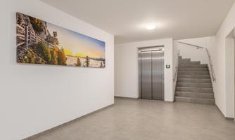 A modern entrance area with a bright wall and a large picture. On the right side, there is an elevator and a staircase.