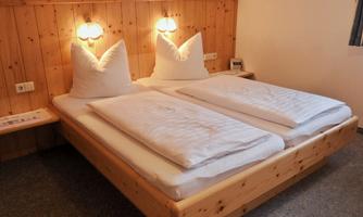 A cozy bedroom with a wooden bed and two high-shaped pillows. The walls are made of wood, and gentle lighting creates a pleasant atmosphere.