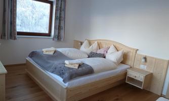 A cozy bedroom with a double bed and light wood details. The window offers a view of a snowy landscape.