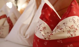 A cozy bed with decorative pillows in red and white. The pillows are adorned with floral patterns.