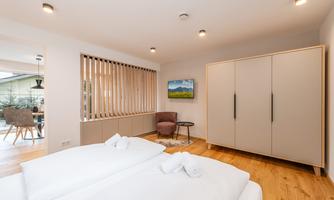 A modern bedroom with two beds and a wardrobe. Additionally, there is a cozy armchair and a view of the outdoor area.