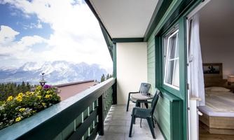 A beautiful balcony with a view of the mountains and a blooming flower plant. The furniture is simple and inviting, perfect for relaxing.