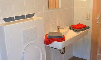 A modern bathroom with a toilet and a sink. Stacked towels are lying on the sink.