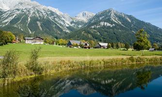 A picturesque landscape with mountains in the background and a tranquil lake in the foreground. Green meadows and traditional buildings complement the harmonious scene.