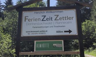 A welcome sign for holiday time Zettler in the forest. It points to holiday apartments and the way to the alpine meadow.