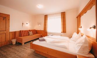 A cozy room with a double bed and an additional sofa bed. Bright walls and wooden furniture create an inviting atmosphere.