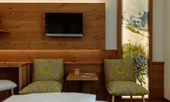 A modern hotel room with wooden paneling. Two comfortably looking armchairs and a television are in the room.