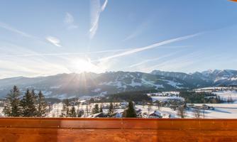 A picturesque winter landscape with snow-covered mountains and a radiant sun. The sky is clear with gentle little clouds.