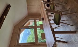 A modern dining room with a large wooden table and chairs. The windows offer a beautiful view of the green landscape and the mountains.