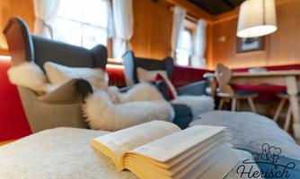 A cozy living area with comfortable chairs and an open book on a sofa. The warm wood tones and soft light create an inviting atmosphere.