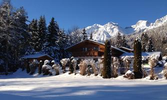 A beautiful house in a snow-covered landscape. In the background, majestic mountains rise under a clear blue sky.
