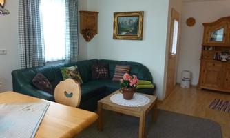 A cozy living room with a green couch and a wooden table. A window with curtains and decorative elements on the walls give the room an inviting atmosphere.