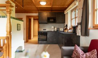 A modern kitchen with black design and wooden ceilings. It is well-equipped with appliances and has a cozy living area next to it.