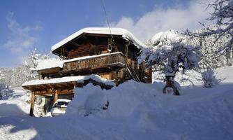 A charming wooden house in the snow with a lovely balcony veranda. The sky is clear and the landscape is wintery lit.
