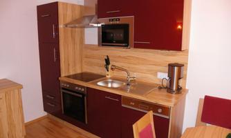 A modern kitchen with red cabinets and wooden fronts. It is well-equipped with a stove, sink, and microwave.
