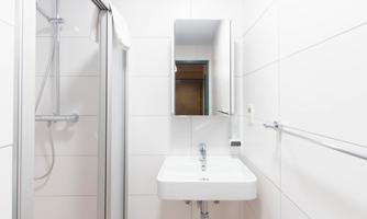 A modern bathroom with white tiles. There is a shower, a sink, and a mirror.
