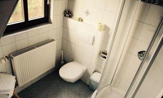 A small bathroom with white tiles and a window. There is a shower, a toilet, and towels on a wooden chair.