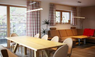 A modern dining area with a large wooden table and elegant chairs. The windows let in plenty of light and create a bright, welcoming atmosphere.
