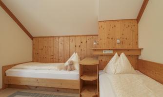 A cozy room with two wooden single beds. The walls are paneled with wood, and a plush toy lies on the bed.