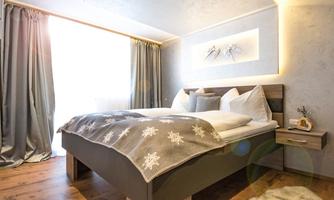 A modern bedroom with a large bed and cozy bedding. The windows let in a lot of light, and the curtains are elegant.