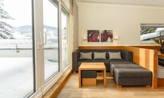 A modern living area with a cozy sofa and a wooden table. A snowy landscape can be seen through the windows.