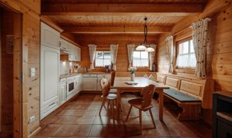 A cozy wooden kitchen with a large table and benches. Bright windows and appealing decorations create an inviting atmosphere.