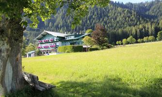 A picturesque country house surrounded by green meadows and mountains. Colorful flowers adorn the balconies of the house.