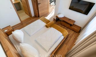 A modern bedroom with a double bed and wooden floor. The room is bright and comfortably furnished, with a television and a seating area.