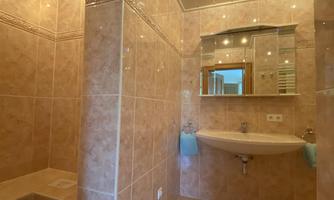 A modern bathroom with bright tiles and a large shower. The space is well-lit and has an elegant sink area.