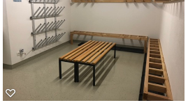 A simple changing room with wooden benches and space for clothing. Coat hooks are attached to the wall.