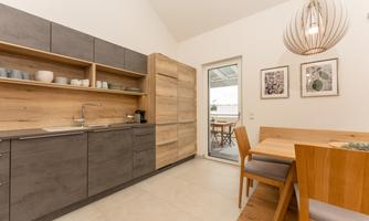 A modern kitchen with wood and gray tones. There is a dining table and a view of an outdoor area.