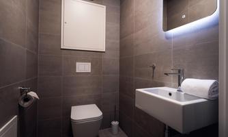 A modern bathroom with gray tiles. It features a toilet, a sink, and a mirror with lighting.